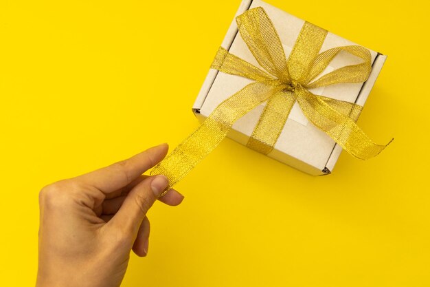 Cropped hand of woman holding gift against yellow background