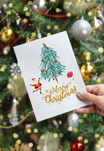 Photo cropped hand of woman holding greeting card against christmas tree