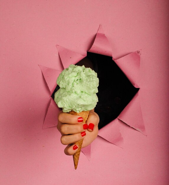 Foto mano tagliata di una donna che tiene un cono di gelato attraverso carta strappata