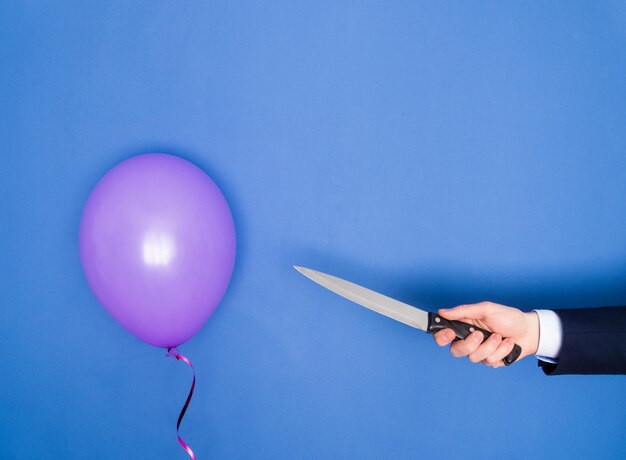 Foto mano tagliata di una donna che tiene un coltello con un palloncino sul tavolo