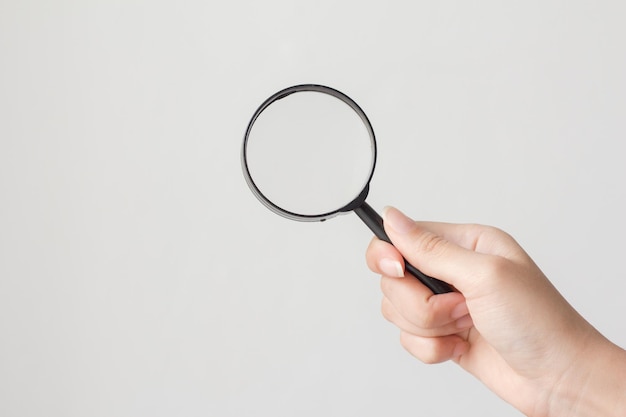 cropped hand of woman holding magnifying glass against white background