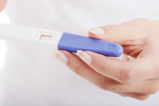 cropped hand of woman holding pregnancy test equipment against white background