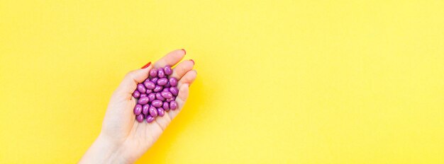 Photo cropped hand of woman holding purple pills against yellow background