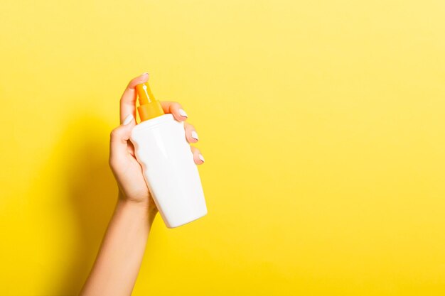 Cropped hand of woman holding shampoo bottle against yellow background