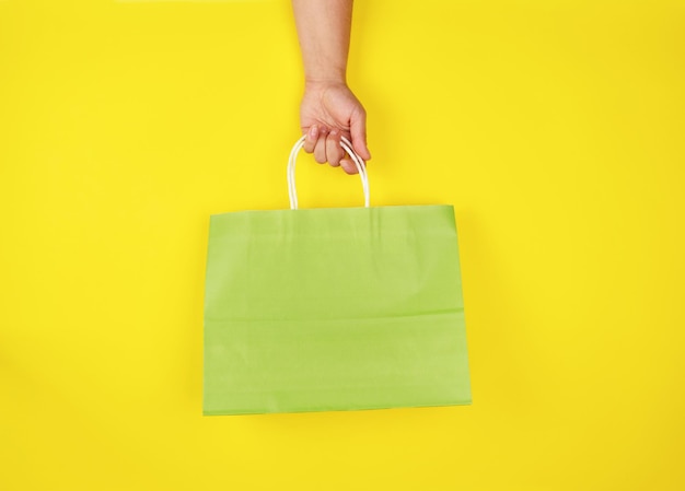 Cropped hand of woman holding shopping bag against yellow background