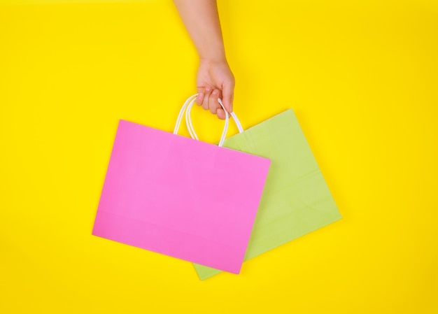 Photo cropped hand of woman holding shopping bags against yellow background