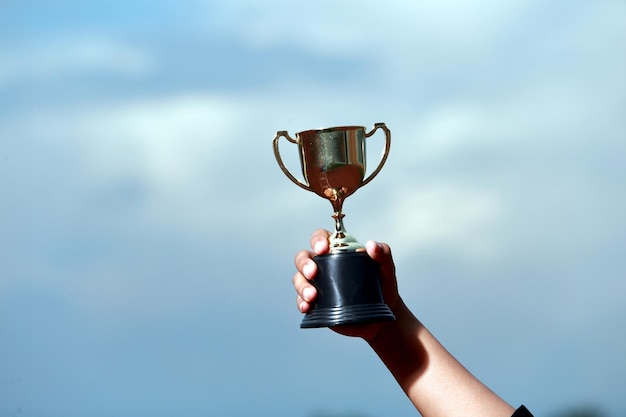 Photo cropped hand of woman holding trophy against sky