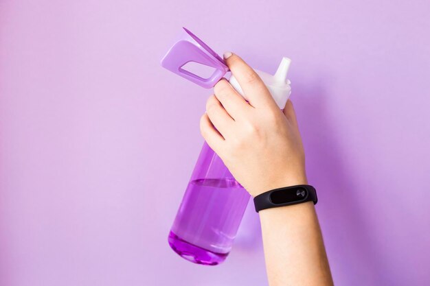 Cropped hand of woman holding water bottle against purple background