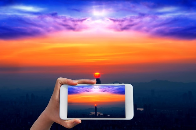 Foto mano tagliata di una donna che fotografa il cielo durante il tramonto