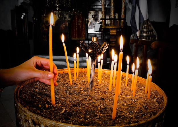 Cropped hand of woman placing lit candle in container at church