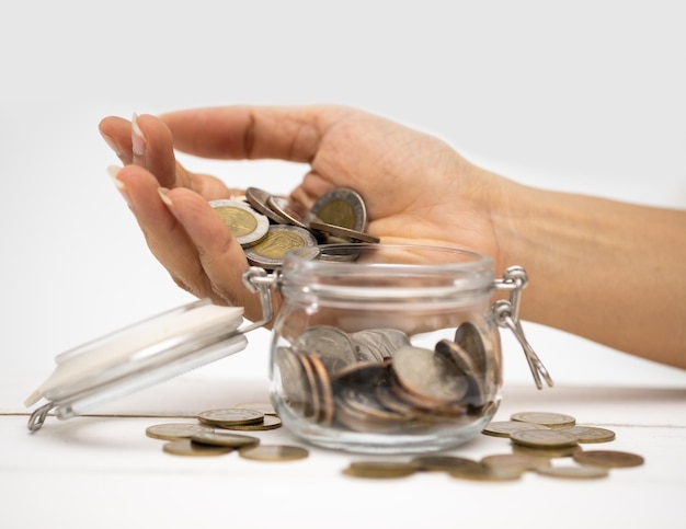 Cropped hand of woman putting coins into glass jar on table