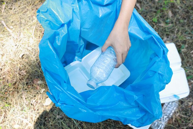 Cropped hand of woman putting water bottle in garbage bag