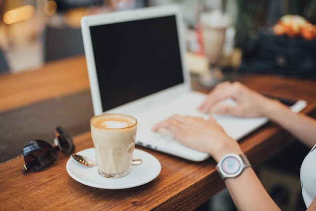 Cropped hand of woman using laptop at cafe