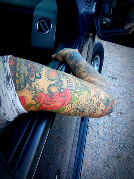 Отрезанная рука женщины с татуировками, сидящей в машине.