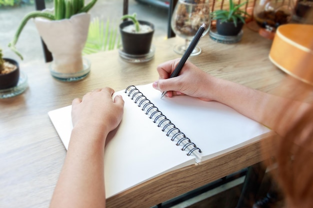 cropped hand of woman writing on blank spiral notebook