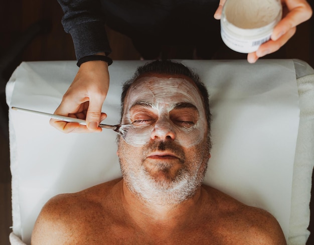 Photo cropped hands applying cream on man face at spa