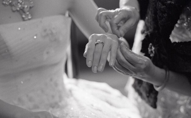 Photo cropped hands of bridesmaid tying thread on bride hand c during wedding