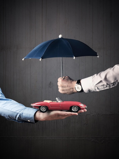 Cropped hands of business people holding toy car and umbrella