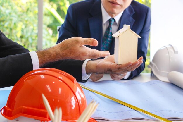 Cropped hands of businessman holding model home while discussing with coworker in office