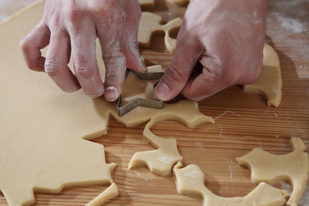 Cropped hands of chef cutting dough with pastry cutter at table