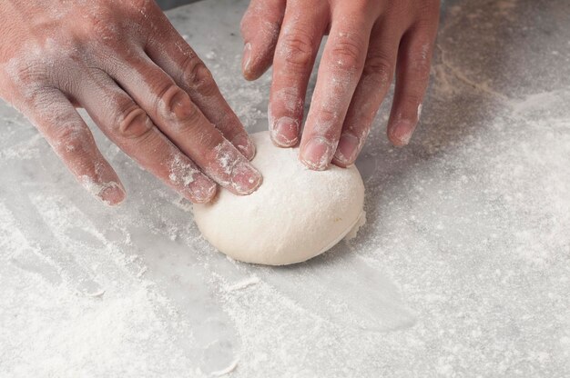 Photo cropped hands of chef kneading dough on table in commercial kitchen