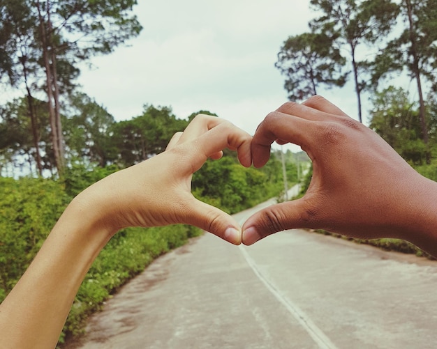 Photo cropped hands of couple making heart shape on road against sky