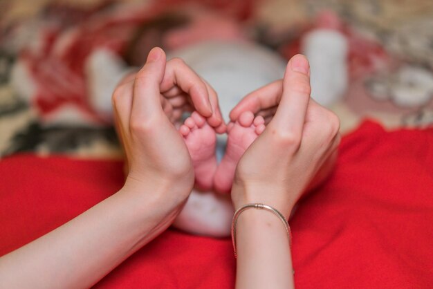 Cropped hands forming heart shape while holding baby feet on bed