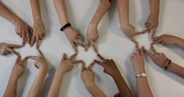 Photo cropped hands of friends forming star shapes with fingers on white table