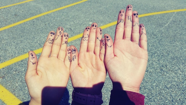 cropped hands of friends with drawing on fingers against road during sunny day