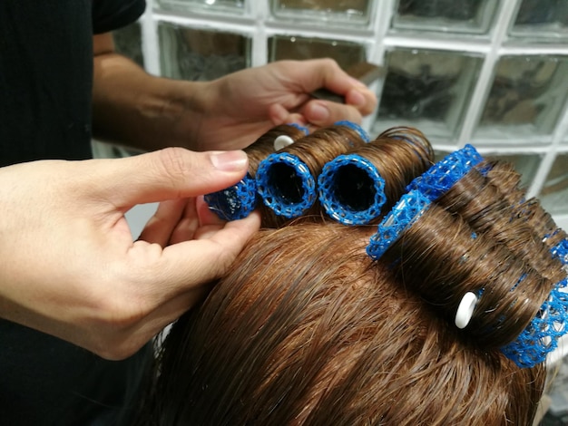 女性にヘアカーラーを塗っているヘアドレッサーの切断された手