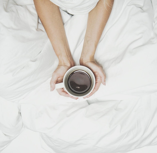 cropped hands holding coffee cup on bed