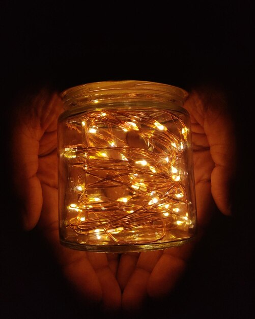 Photo cropped hands holding jar with illuminated string lights in darkroom