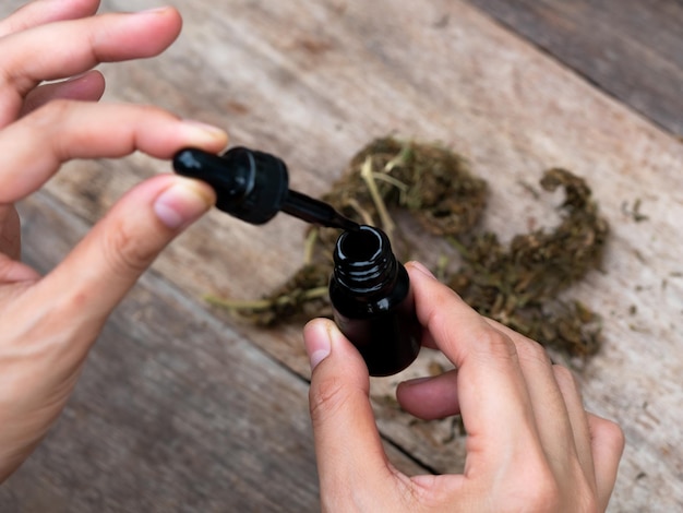 cropped hands holding liquid over marijuana at table