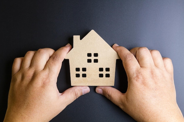 Cropped hands holding wooden house toy on gray background