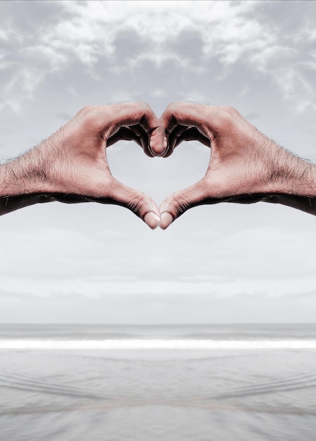 Руки, сделанные в форме сердца на пляже на фоне неба.