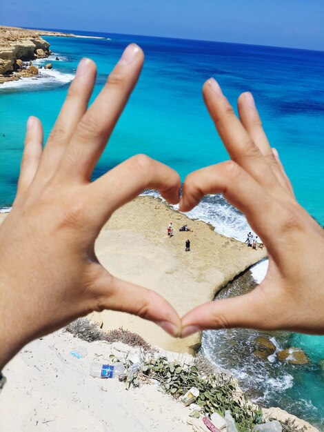 Foto mani tagliate che fanno forma di cuore sulla spiaggia durante una giornata di sole