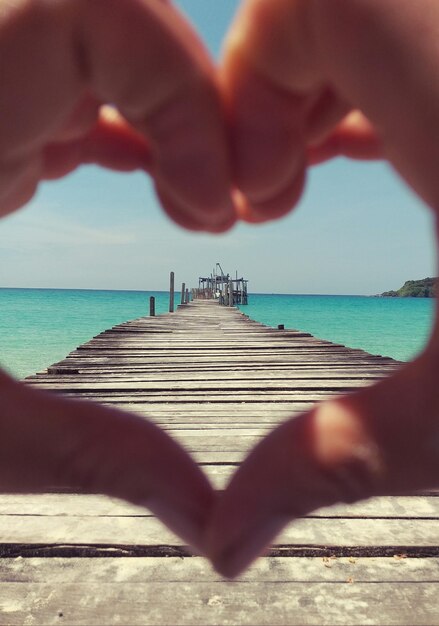 Photo cropped hands making heart shape by sea at pier