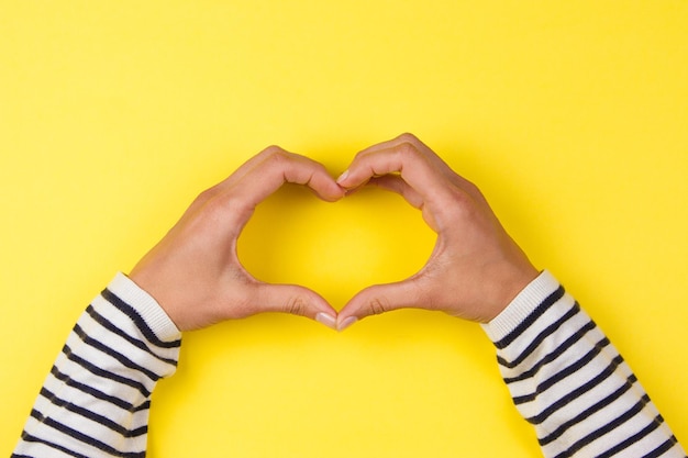 Foto mani tagliate che fanno forma di cuore su uno sfondo giallo