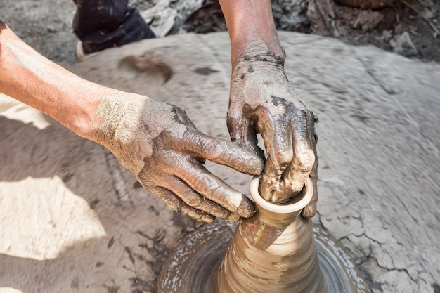 cropped hands of male potter making pot on field