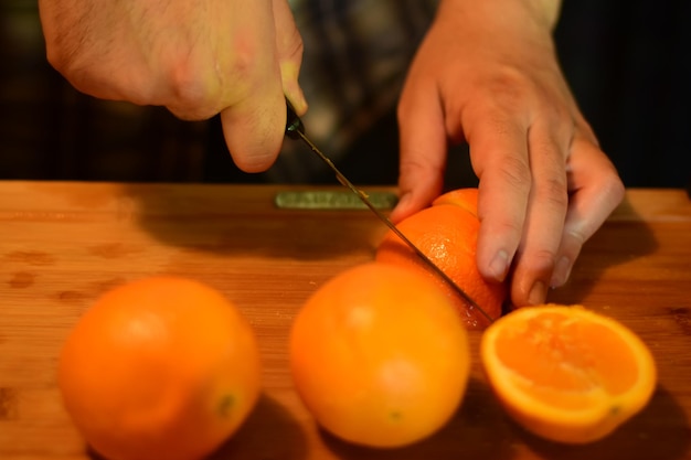 Photo cropped hands of man cutting orange fruits on table