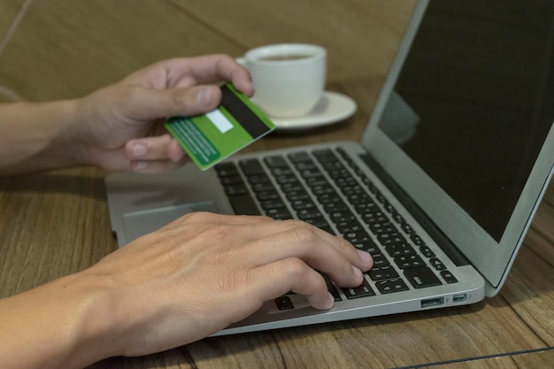 Photo cropped hands of man holding credit card while using laptop for online shopping on table