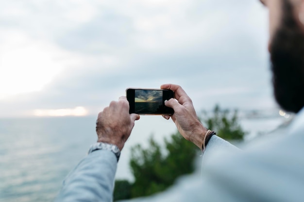 Photo cropped hands of man photographing sea from mobile phone