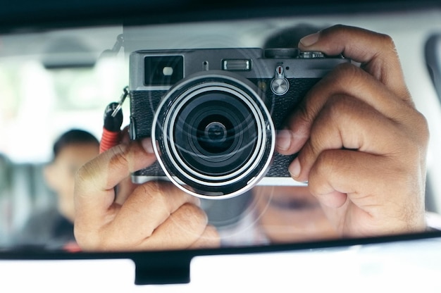 Photo cropped hands of man photographing with camera reflecting on rear-view mirror in car