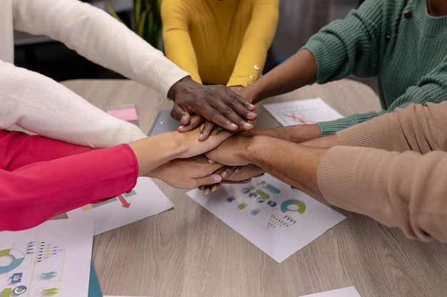 Cropped hands of multiracial male and female advisors stacking hands over conference table in office