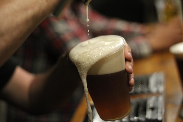 Фото Урезанные руки человека, наливающего пиво в стакан.