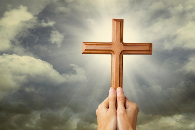 Фото Обрезанные руки человека, держащего деревянный религиозный крест на облачном небе