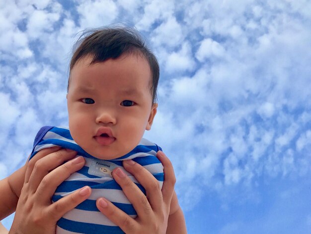 Cropped hands of parent holding baby boy against sky