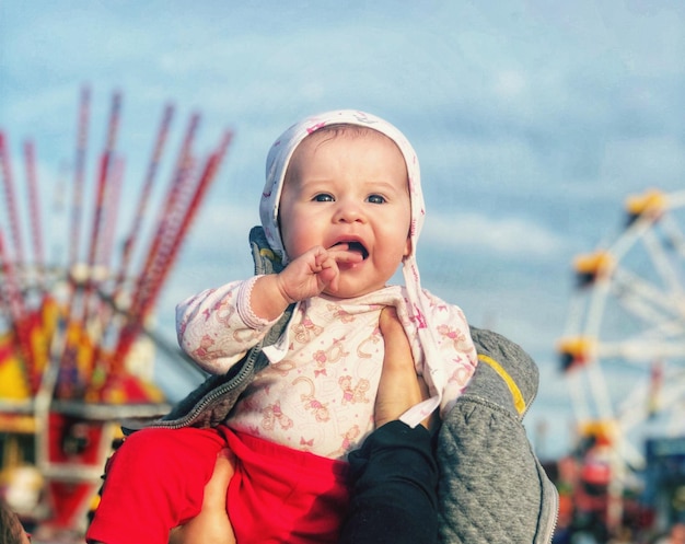 Foto mani tagliate di un genitore che tiene una bambina contro il cielo