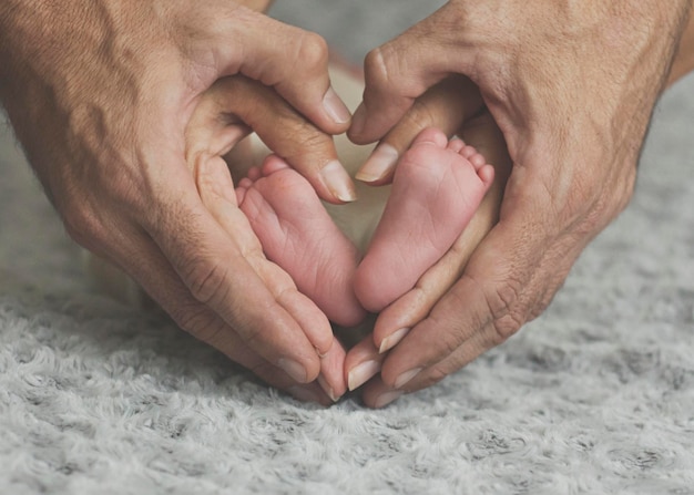 cropped hands of parents forming heart shape around baby feet