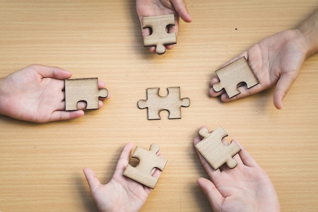 Cropped hands of people holding jigsaw pieces on table